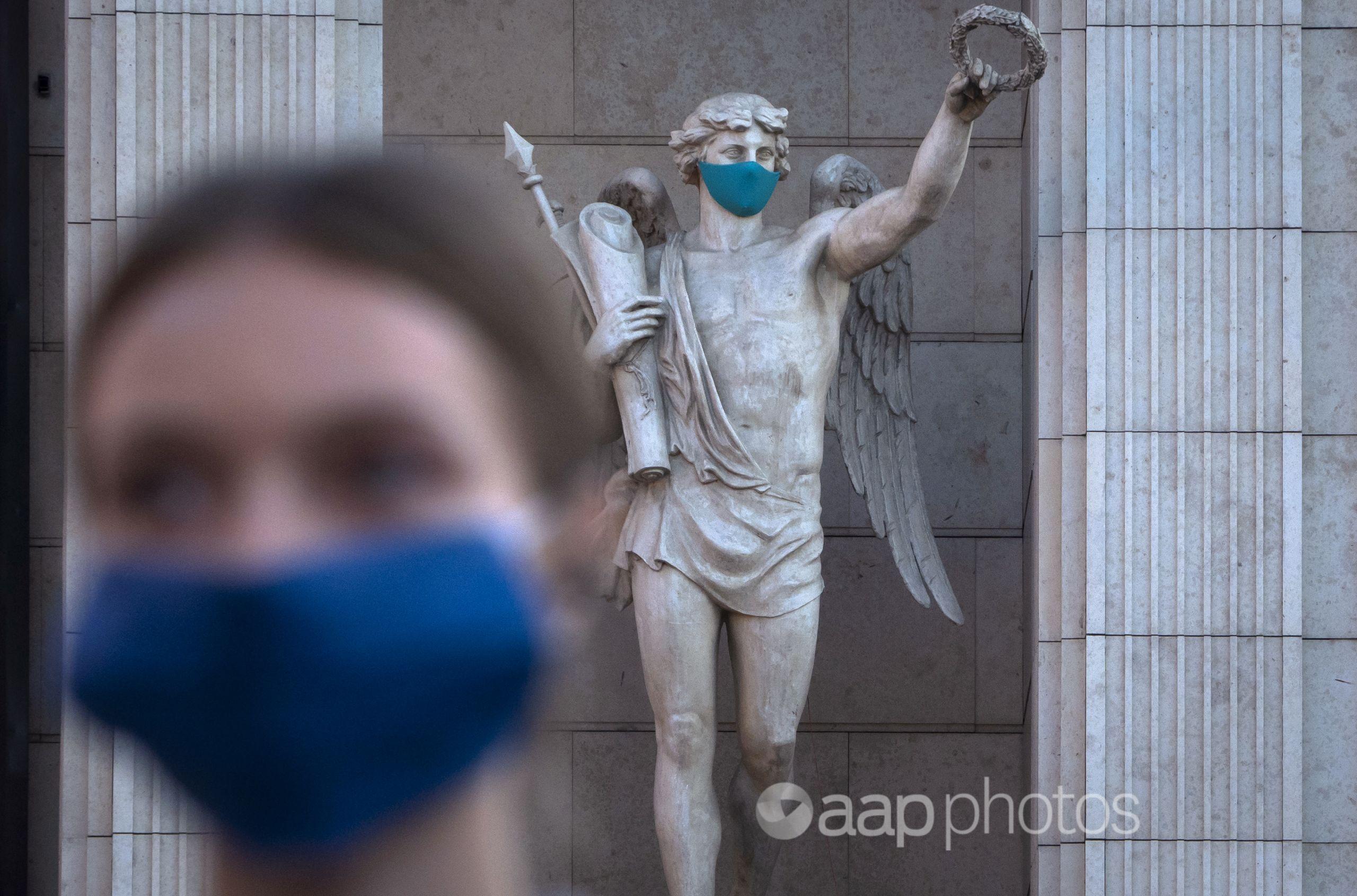 A woman wearing a face mask walks past a statue with a face mask.
