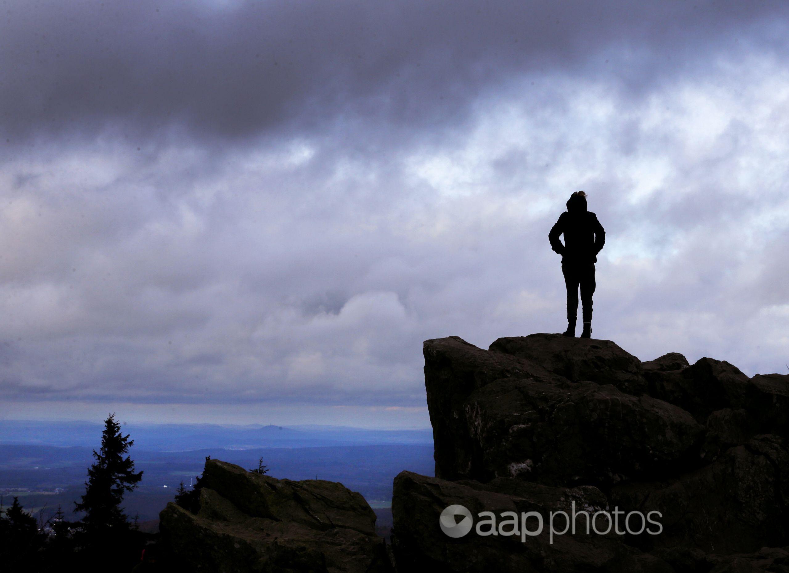A woman stands on rocks on top of a mountain.