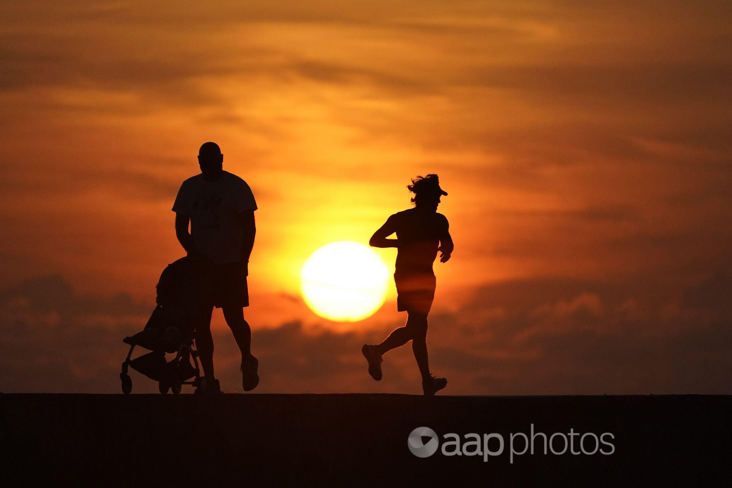 runner, man pushing pram silhouetted against a sunrise