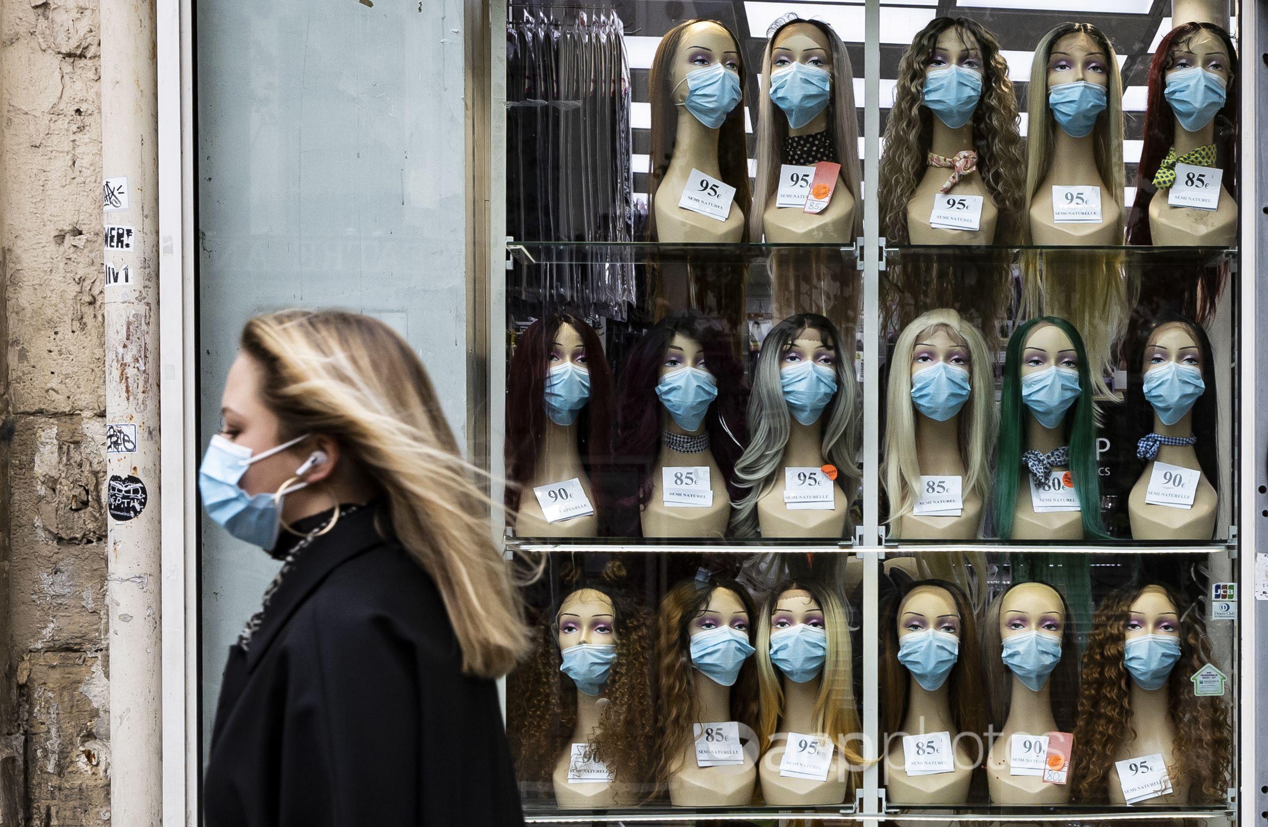 A woman wearing a face mask walks past a shop displaying masks