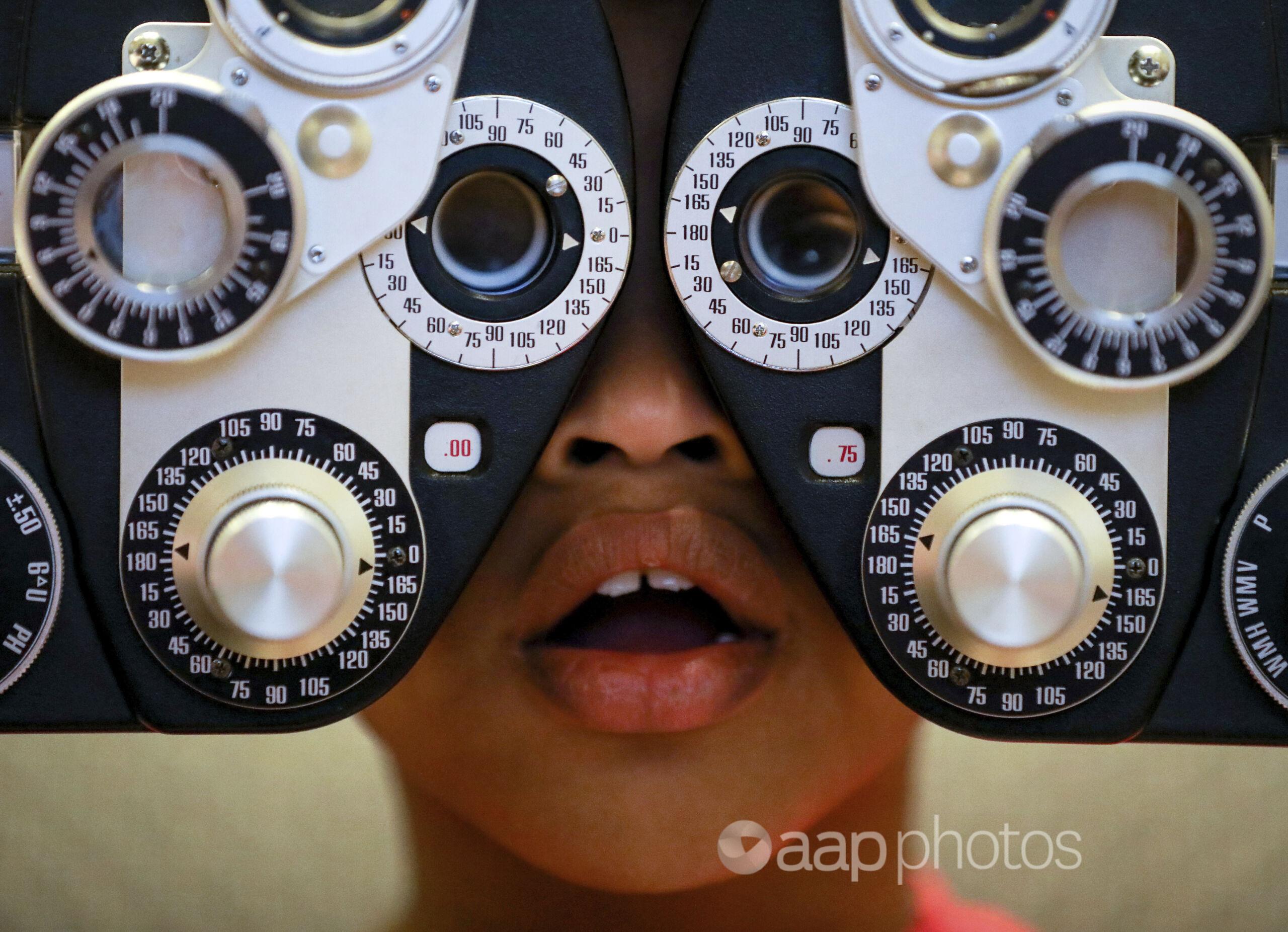 A boy looks through a phoropter to assess his vision for new glasses.