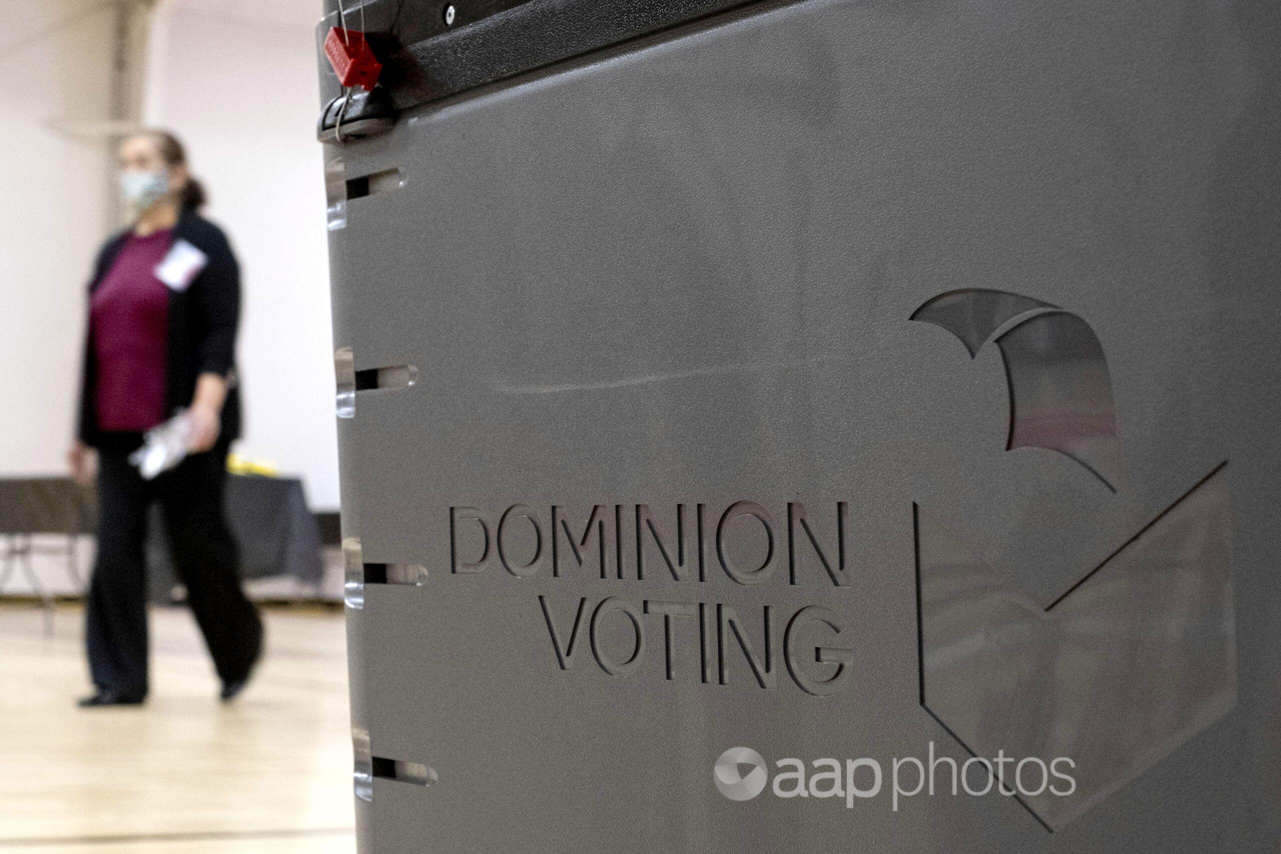 A worker passes a Dominion Voting ballot scanner.