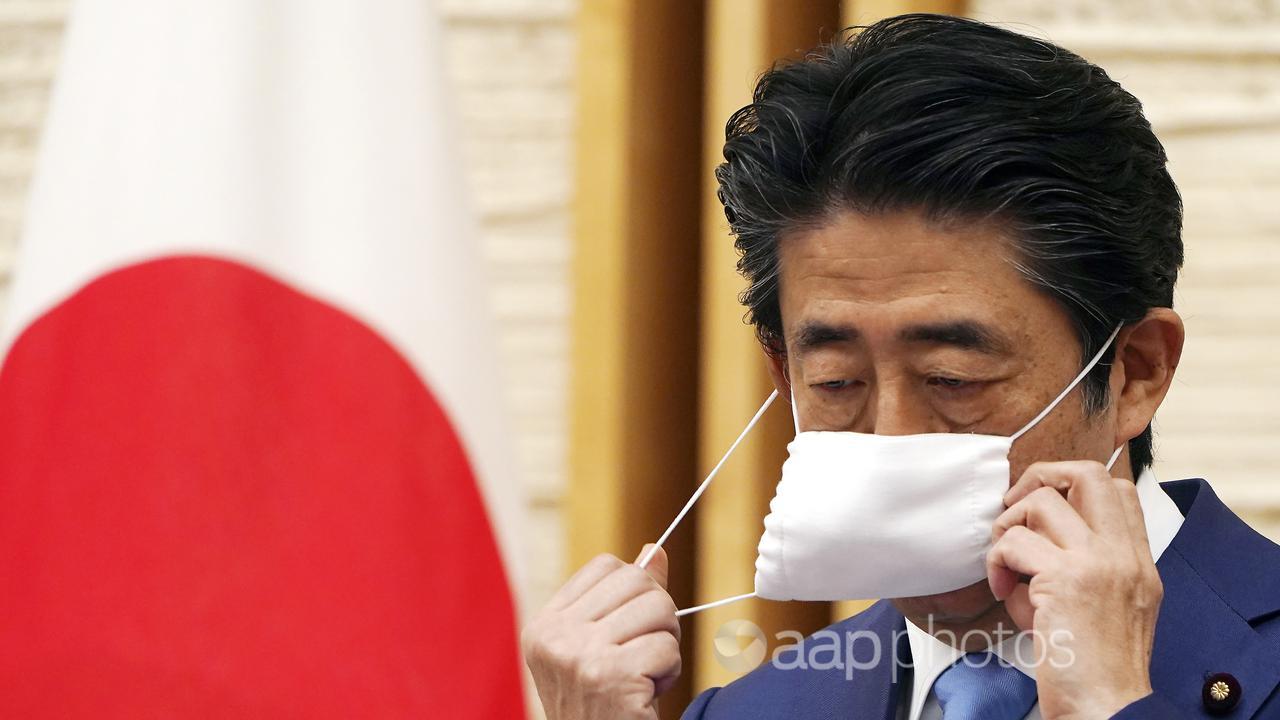 Former Japanese prime minister Shinzo Abe removes a face mask.