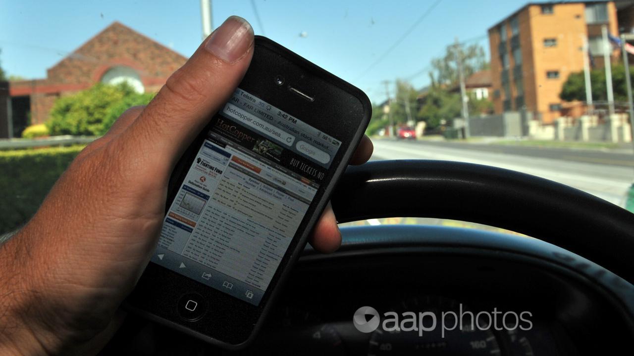 A driver holds a mobile phone while behind the wheel. 