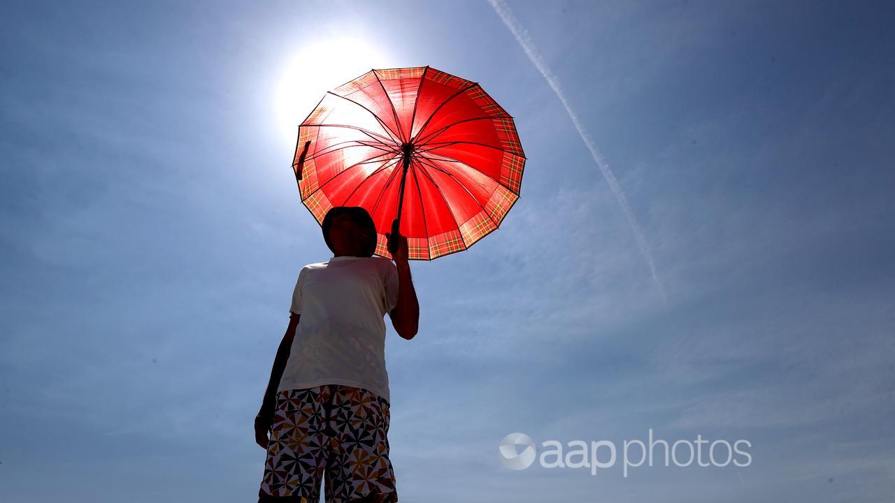 A man walks with an umbrella during hot weather