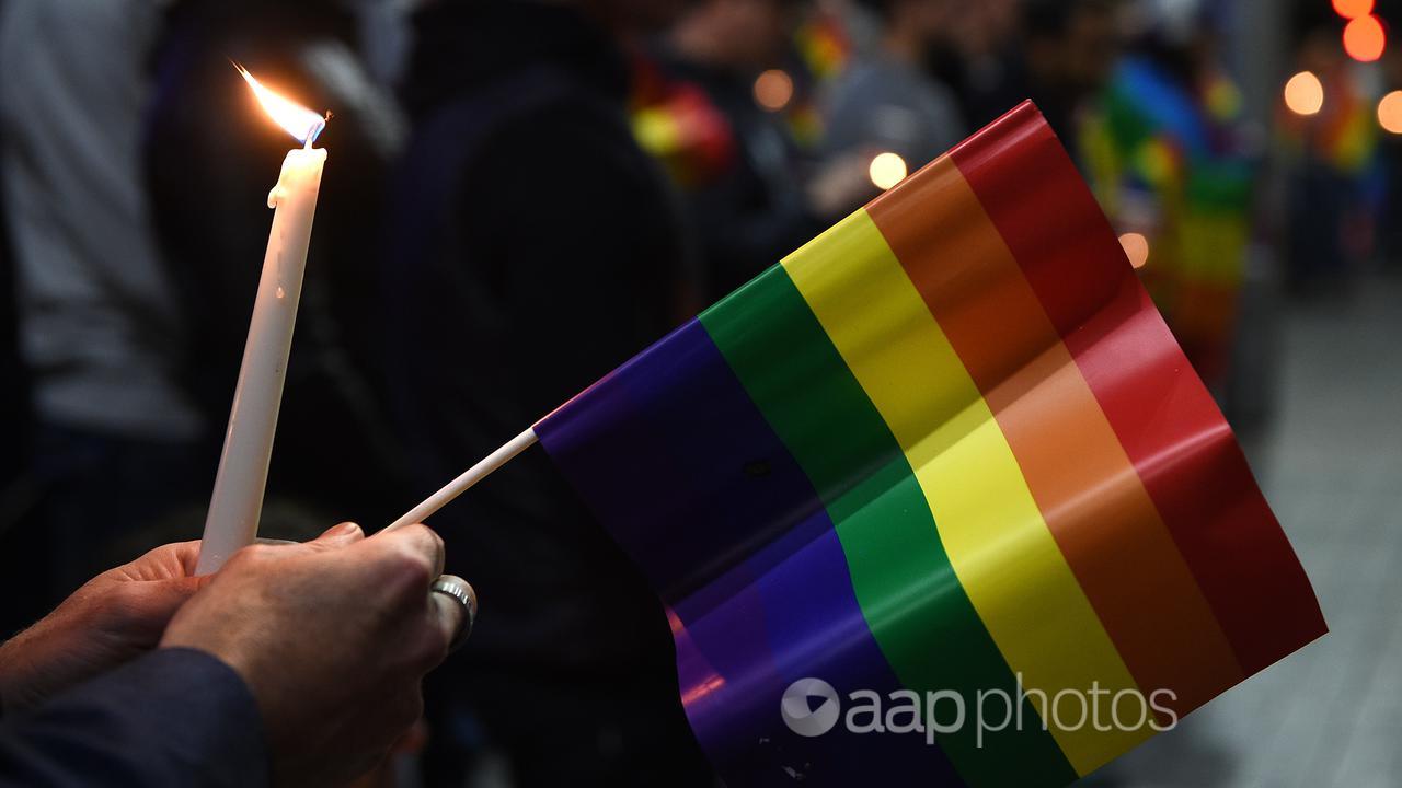 A person holds a candle and a rainbow flag