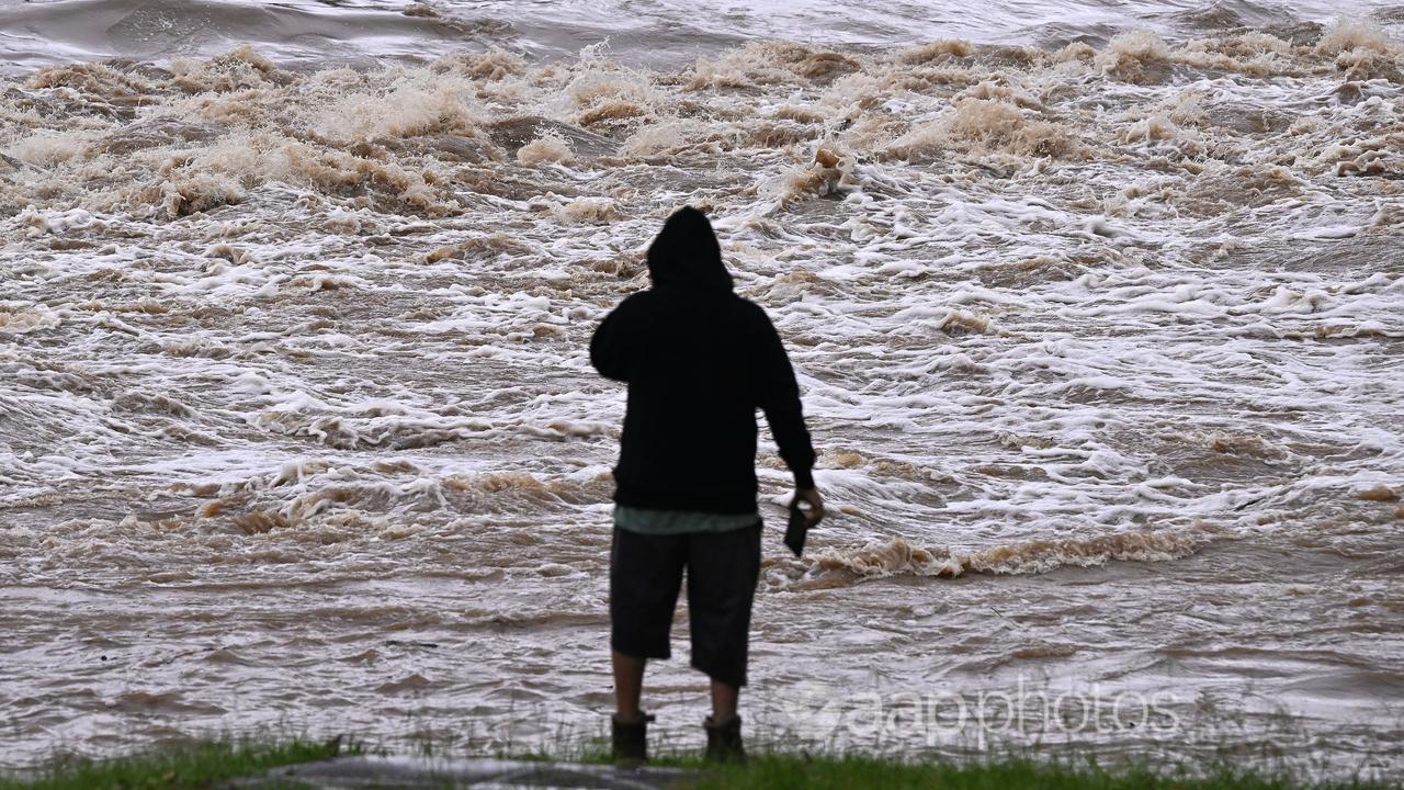 A man watches a river swollen by floodwaters.
