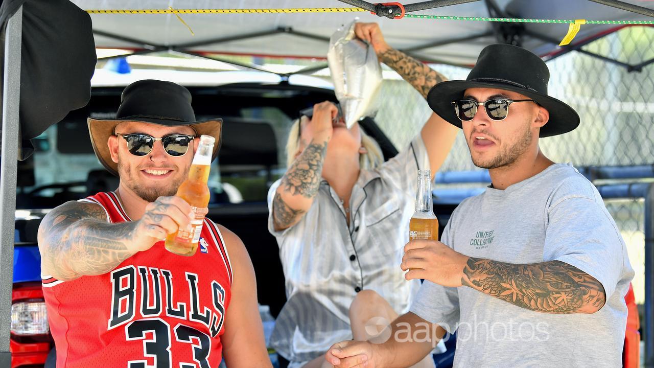 Two men drink beer under a shade cloth