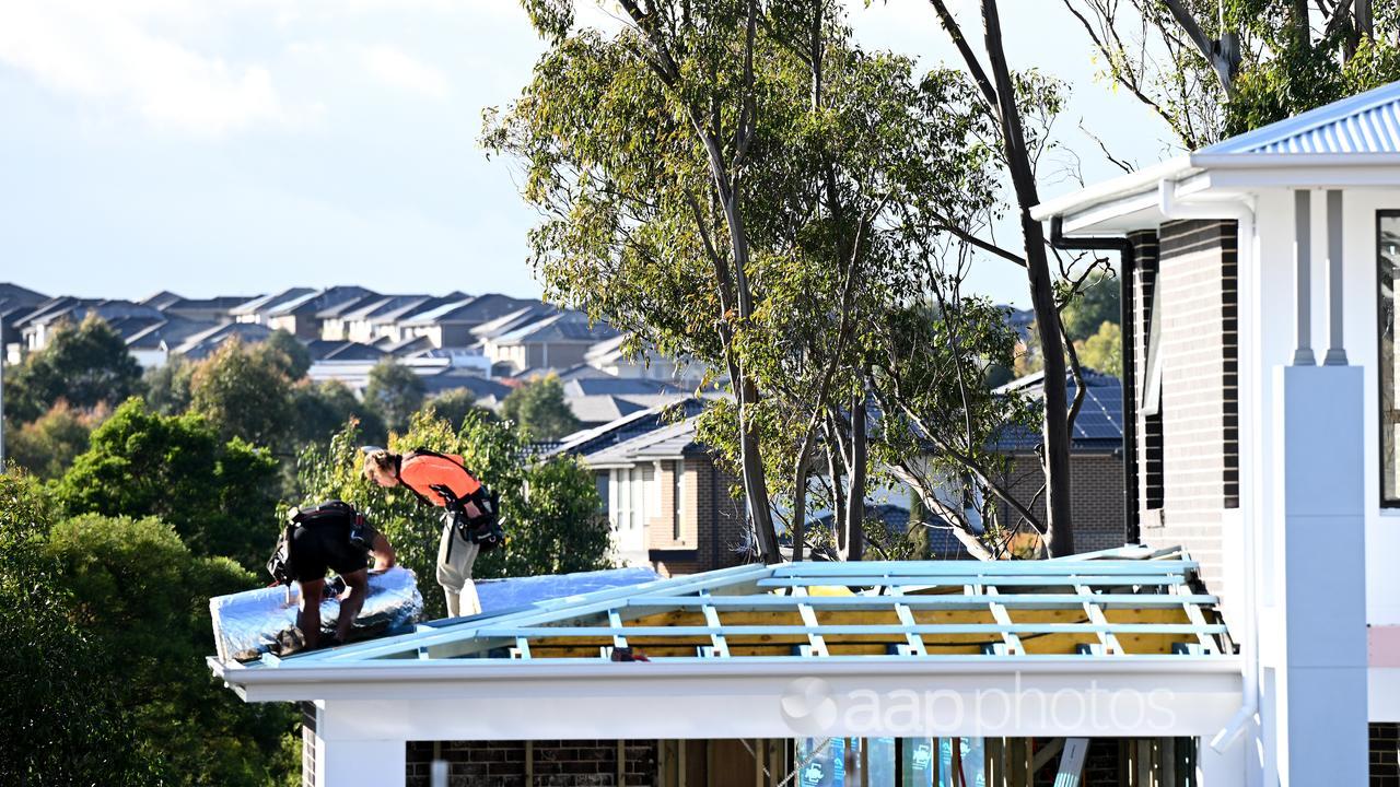 People work on a house roof with more homes in the background.