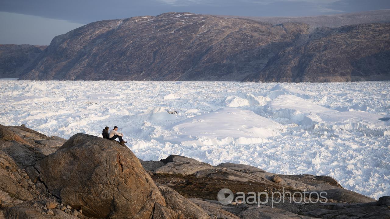 Student researchers sit on a rock overlooking a glacier in Greenland