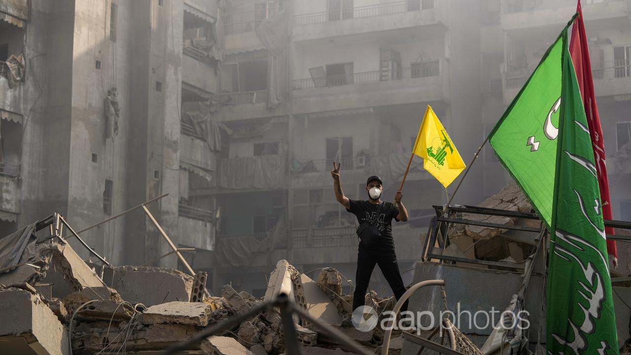 A man holding up a Hezbollah flag amid ruins in Lebanon.